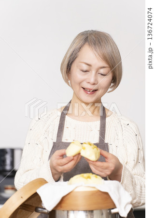 キッチンでさつま芋の蒸しパンをせいろで蒸して作るシニア女性 136724074