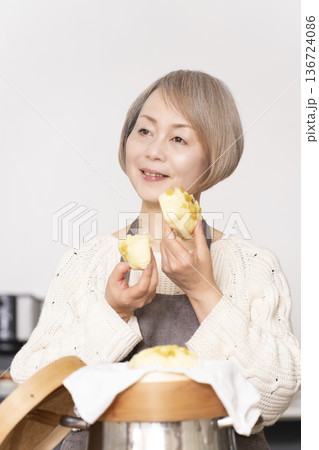 キッチンでさつま芋の蒸しパンをせいろで蒸して作るシニア女性 キッチンでさつま芋の蒸しパンをせいろで蒸して作るシニア女性 136724086