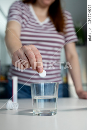 Woman Dropping an Effervescent Tablet Into a Glass of Water on a Kitchen Counter Woman Dropping an Effervescent Tablet Into a Glass of Water on a Kitchen Counter 136724092