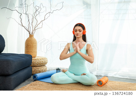 Woman sits on a mat with headphones, practicing yoga focus 136724180