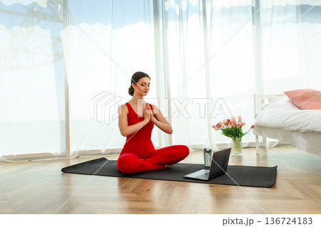 A woman sits on a mat with hands together in a yoga pose A woman sits on a mat with hands together in a yoga pose 136724183