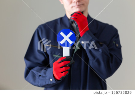 バツのプレートを持って悩む作業服のミドル男性ビジネスマン バツのプレートを持って悩む作業服のミドル男性ビジネスマン 136725829