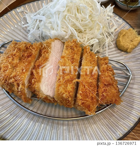 Crispy tonkatsu, a Japanese-style breaded and deep-fried pork cutlet, served with shredded cabbage and drizzled with savory sauce. A delightful balance of crunchy texture and juicy meat. 136726971