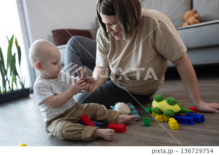 Engaged Baby Explores With Vibrant Toys During Nurturing Play Activity Supervised By Mother Engaged Baby Explores With Vibrant Toys During Nurturing Play Activity Supervised By Mother 136729754