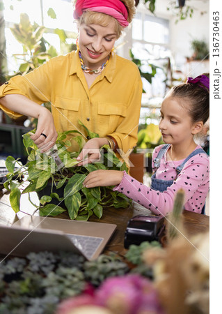 A woman and a young girl are working together to prune a houseplant, enjoying a moment of connection A woman and a young girl are working together to prune a houseplant, enjoying a moment of connection 136730463