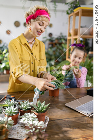 A woman and child are tending to plants in a bright, inviting indoor setting A woman and child are tending to plants in a bright, inviting indoor setting 136730495
