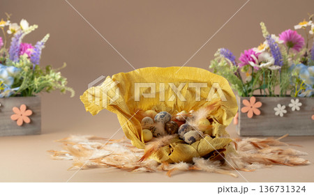 Crepe paper nest with quail eggs, feathers, and spring flowers on a beige background. Crepe paper nest with quail eggs, feathers, and spring flowers on a beige background. 136731324