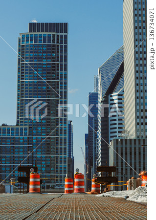 Construction work takes place in a city area filled with tall buildings during a sunny day Construction work takes place in a city area filled with tall buildings during a sunny day 136734071