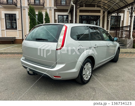 Silver car parked in front of a building with a simple design and garden on a cloudy day in a residential area Silver car parked in front of a building with a simple design and garden on a cloudy day in a residential area 136734123