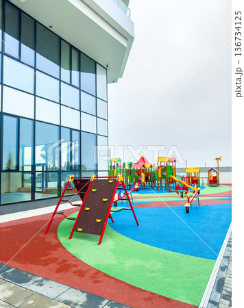 Colorful playground with climbing frame and slides located near a modern building in an urban area during cloudy weather 136734125