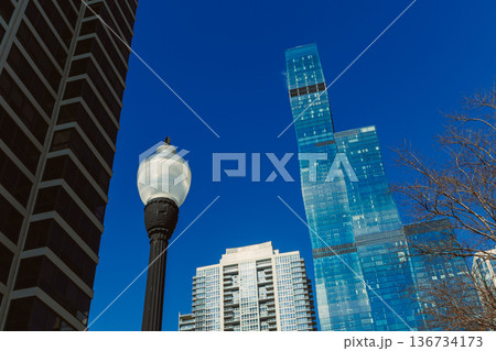 Tall glass building stands next to older structure under clear blue sky with street lamp in foreground during daytime at urban location 136734173