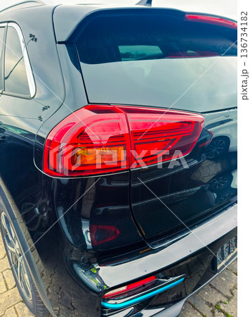Black vehicle parked in a public space with focus on rear light and bumper captured in the afternoon with visible reflections 136734182