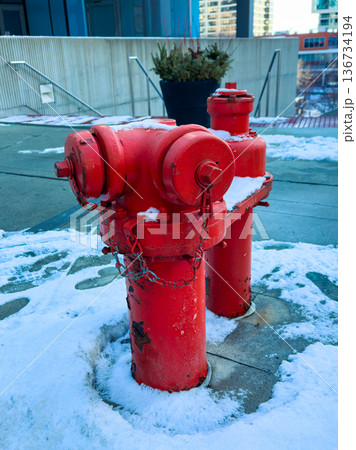 Red fire hydrant covered with snow beside a building in a city during winter season 136734194
