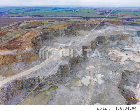 Large quarry site showing excavation work and heavy machinery in a rural area under cloudy skies 136734204