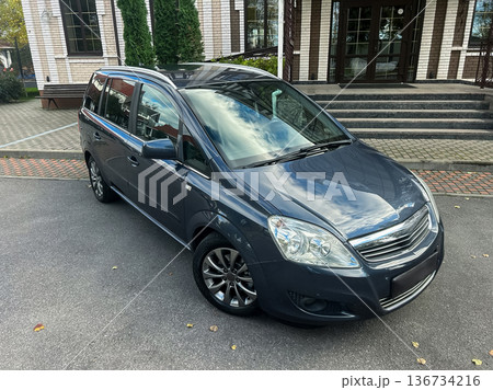 Shiny gray minivan parked near an elegant building surrounded by trees on a clear day, showcasing its sleek design and modern features Shiny gray minivan parked near an elegant building surrounded by trees on a clear day, showcasing its sleek design and modern features 136734216