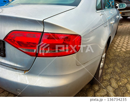 Damaged silver car parked in a lot with multiple vehicles and clear blue sky in the background during the day 136734235