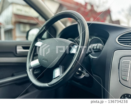 Car interior shows steering wheel with dashboard and controls in a parked vehicle during a sunny day Car interior shows steering wheel with dashboard and controls in a parked vehicle during a sunny day 136734238