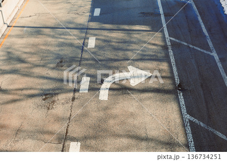 Road sign showing a right turn on a city street during daylight with shadows on the pavement 136734251
