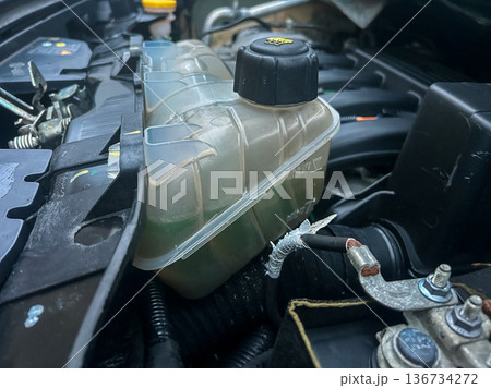 Engine coolant reservoir located in a car's engine compartment showing fluid levels and components 136734272