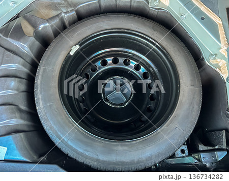 Spare tire located in the trunk of a car at a service station during daytime to prepare for any roadside emergencies Spare tire located in the trunk of a car at a service station during daytime to prepare for any roadside emergencies 136734282