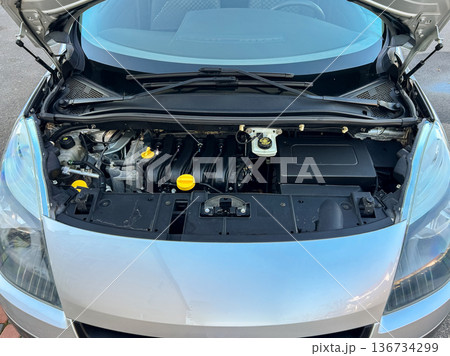 Engine view of a compact car showing the mechanical components, cooling system, and battery location in a parking area during daytime Engine view of a compact car showing the mechanical components, cooling system, and battery location in a parking area during daytime 136734299