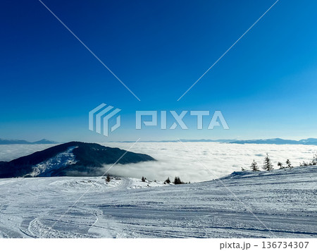 Clouds cover the landscape while snow rests on the mountains during a clear winter day in a ski resort Clouds cover the landscape while snow rests on the mountains during a clear winter day in a ski resort 136734307