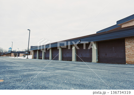 Storage units in a commercial building on a cloudy day with empty parking space and minimal activity visible Storage units in a commercial building on a cloudy day with empty parking space and minimal activity visible 136734319