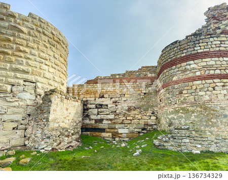 Historic stone ruins stand in an open area with grass and clear sky in the background during the daytime around a historical site 136734329