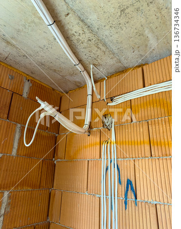 Electrical wires and pipes installed in a construction site corner of a room during renovation work 136734346