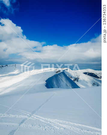 Snow-covered hills under a clear blue sky with some clouds in the background this winter scene shows a serene landscape of nature and cold weather 136734353