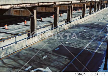 Empty highway beneath a structure with traffic cones in a city during daylight hours Empty highway beneath a structure with traffic cones in a city during daylight hours 136734354