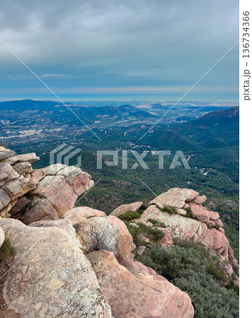 View of a valley from a rocky viewpoint on a mountain in the early evening with clouds overhead and distant hills in sight View of a valley from a rocky viewpoint on a mountain in the early evening with clouds overhead and distant hills in sight 136734366