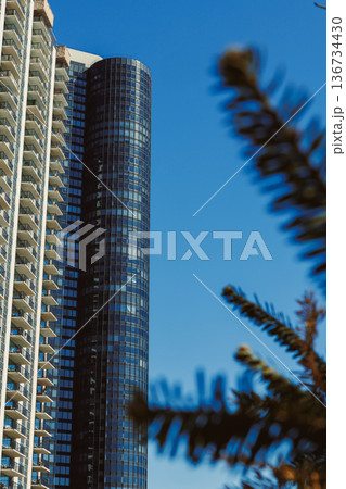 Tall building stands next to residential structure under clear blue sky on a sunny day in a city setting 136734430