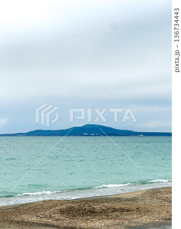 Cloudy skies above the water with distant mountains and shoreline during the day near a beach location Cloudy skies above the water with distant mountains and shoreline during the day near a beach location 136734443