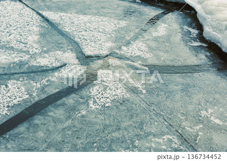 Cracked ice reflects light in a frozen lake during winter showing patterns and textures on the surface Cracked ice reflects light in a frozen lake during winter showing patterns and textures on the surface 136734452