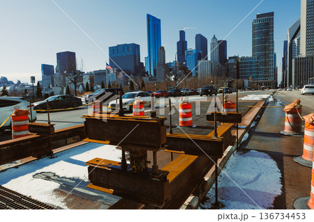 Construction work occurs on a city road with barriers in Chicago during winter under a clear sky with tall buildings in the background Construction work occurs on a city road with barriers in Chicago during winter under a clear sky with tall buildings in the background 136734453