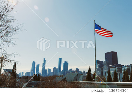 City skyline with American flag flying on a clear day in the background of tall buildings and open sky City skyline with American flag flying on a clear day in the background of tall buildings and open sky 136734504