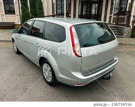 Silver car parked outside a building, showcasing its rear view on a cloudy day with trees in the background 136734516
