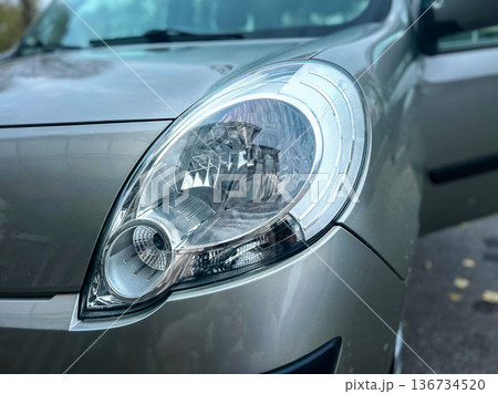Close up view of a car headlight with open door and shiny surface in an urban area during daylight hours Close up view of a car headlight with open door and shiny surface in an urban area during daylight hours 136734520