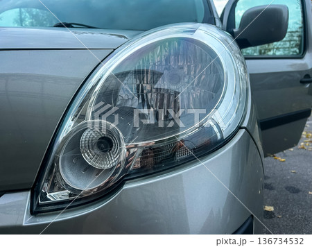 Close view of a car headlight with the car door open showing the interior and an outdoor setting during daylight 136734532