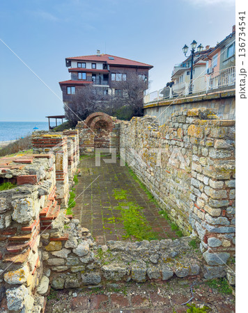 Ruins of an ancient structure near the sea with a modern building in the background on a sunny day Ruins of an ancient structure near the sea with a modern building in the background on a sunny day 136734541
