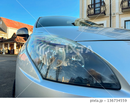 Car headlight shines bright in a clear sky near a building in an urban area during daytime Car headlight shines bright in a clear sky near a building in an urban area during daytime 136734559