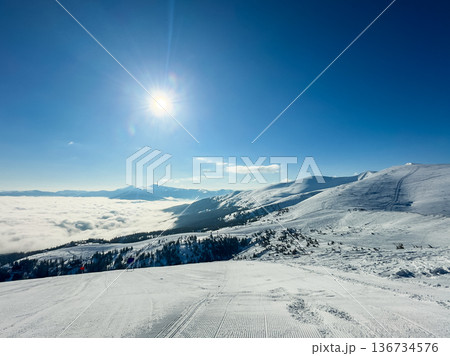 Snow-covered mountain landscape with clear sky and sun shining above the clouds in early afternoon 136734576