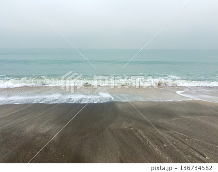 Waves roll onto the shore at a quiet beach during early morning hours with soft gray skies above Waves roll onto the shore at a quiet beach during early morning hours with soft gray skies above 136734582