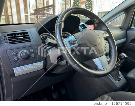 Driver's view inside a car showing steering wheel and dashboard in a parking space during daytime 136734596