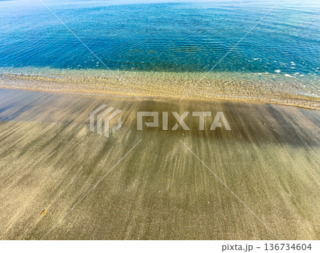 Calm water meets sandy shore on a sunny day at the beach with gentle waves in the afternoon light Calm water meets sandy shore on a sunny day at the beach with gentle waves in the afternoon light 136734604