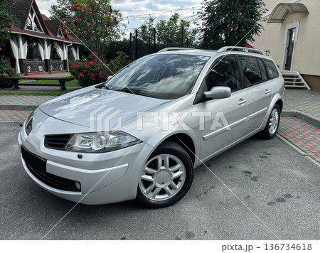 Sleek silver car parked in a charming garden setting with a cozy house and blooming flowers nearby, under a bright blue sky on a sunny afternoon 136734618