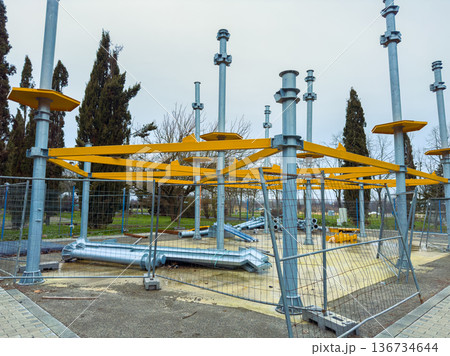 Construction of a new playground structure in a public park with metal frames and safety barriers set up for community use during cloudy weather 136734644