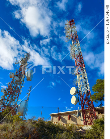 Two tall communication towers standing against a blue sky with clouds in a remote area during daylight Two tall communication towers standing against a blue sky with clouds in a remote area during daylight 136734649