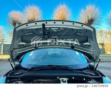 Car hood is open and engine area is visible during daytime at a parking area with trees in the background Car hood is open and engine area is visible during daytime at a parking area with trees in the background 136734650